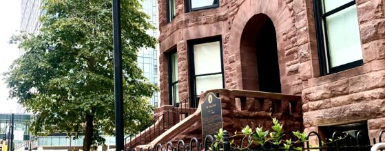 Madonna the Great Dane sitting on the 9th Street sidewalk in front of the restored 1889 Oakland's on 9th brownstone in downtown Minneapolis, summer flowers along the fence