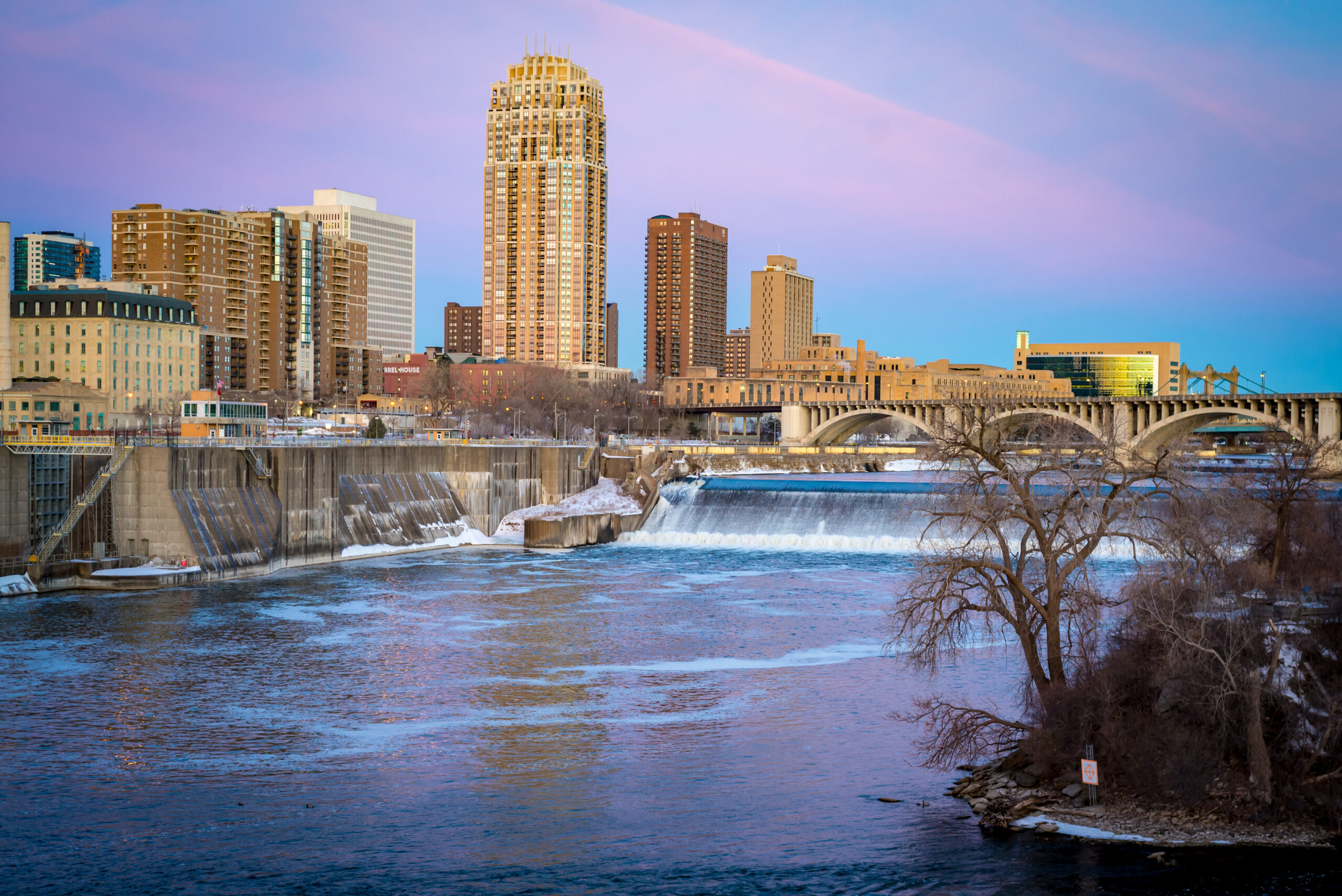 View of the downtown Minneapolis skyline and the Mississippi River seen from the Stone Arch Bridge on a clear day.