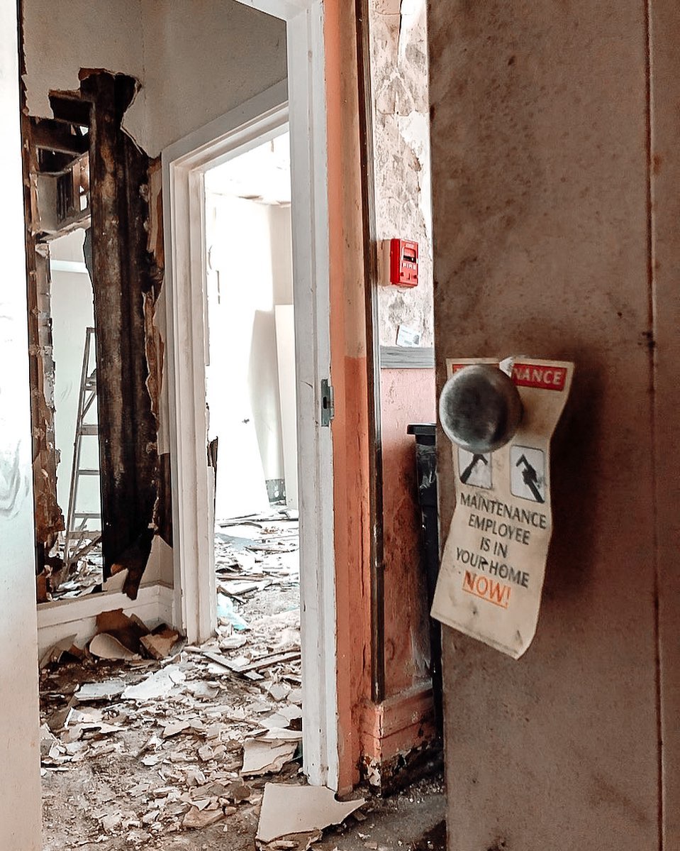 The fire-damaged interior of the Oaklands before restoration: a gutted room with debris, peeling plaster, and an old maintenance door hanger.