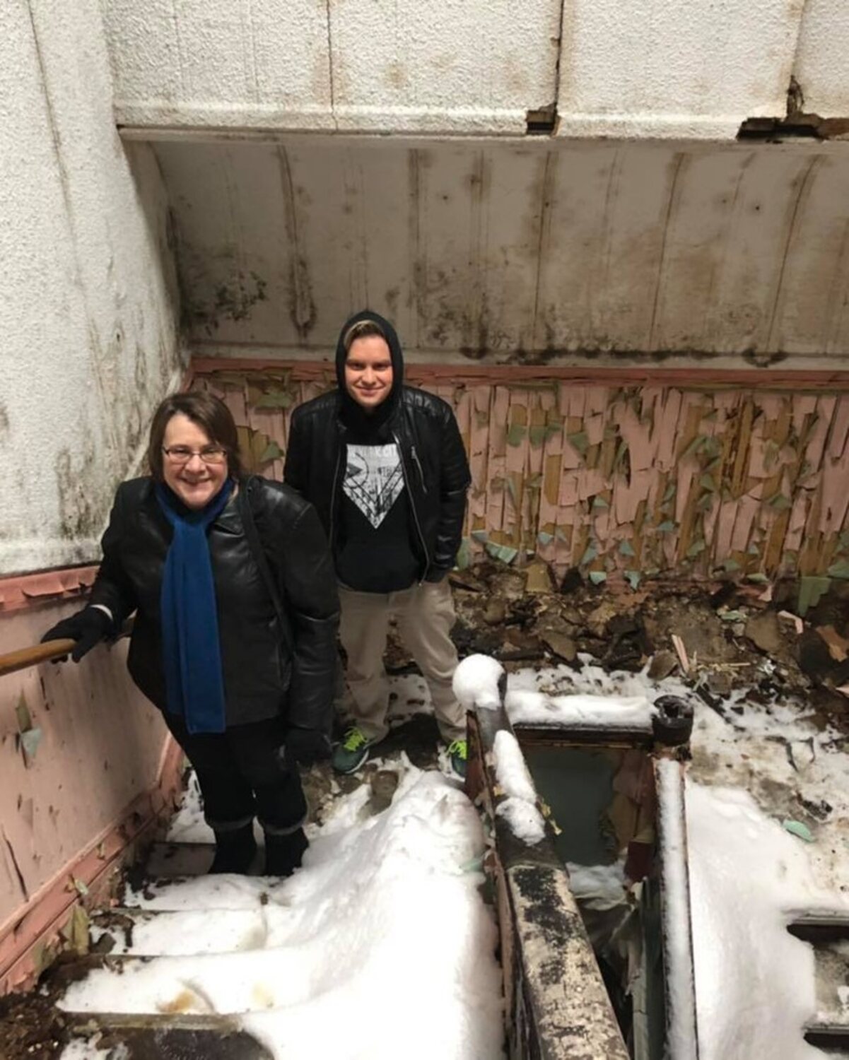 Two people stand in a snow-filled, peeling interior room of Oaklands on 9th during the years it sat roofless after the 2016 fire.