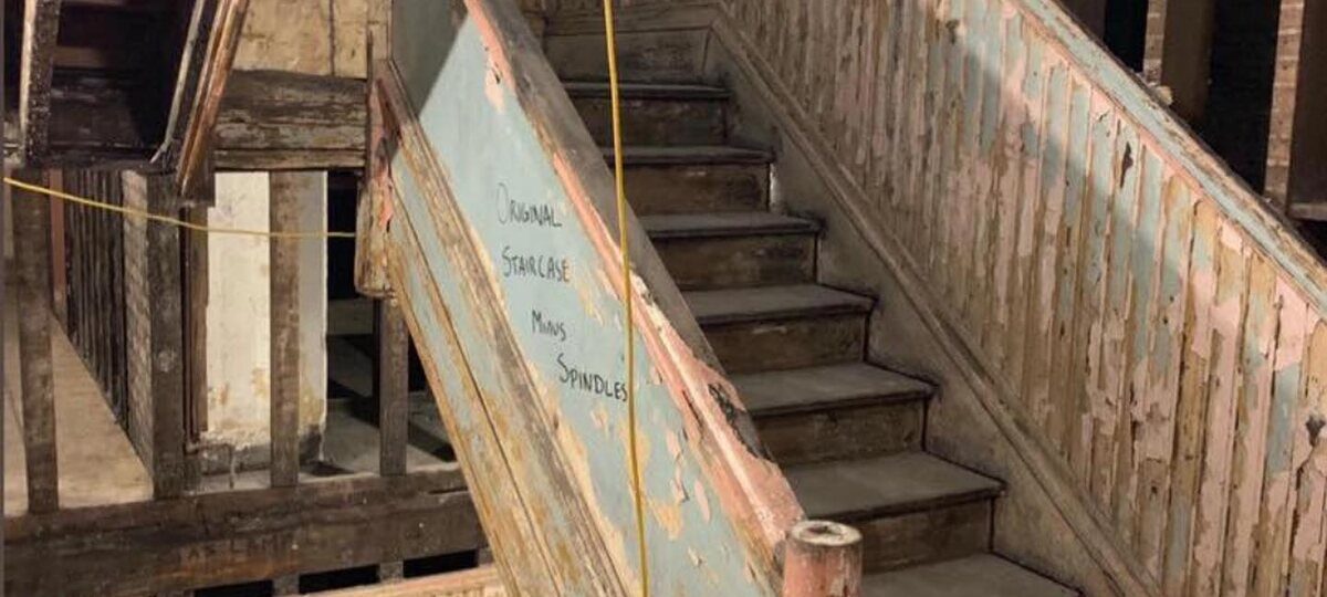 The Oaklands on 9th grand staircase mid-restoration, stripped to bare weathered wood after three winters exposed to the open sky.
