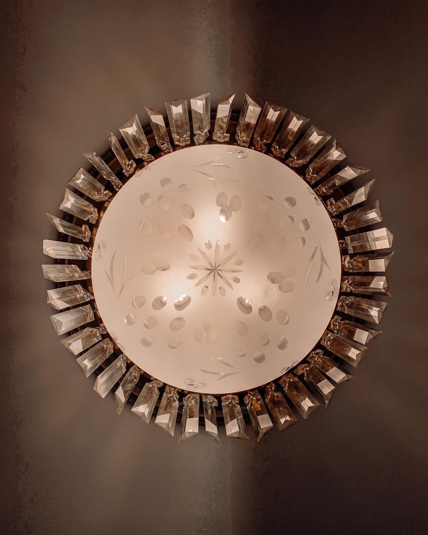 A restored flush-mount ceiling light at Oaklands on 9th, with an etched glass shade ringed by faceted glass prisms, seen from below.