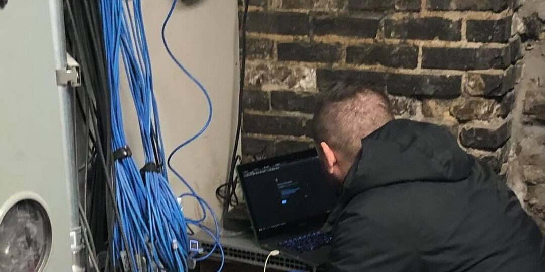 Technician splicing fiber internet in the 1889 coal room at Oaklands on 9th, cables running across original brick walls