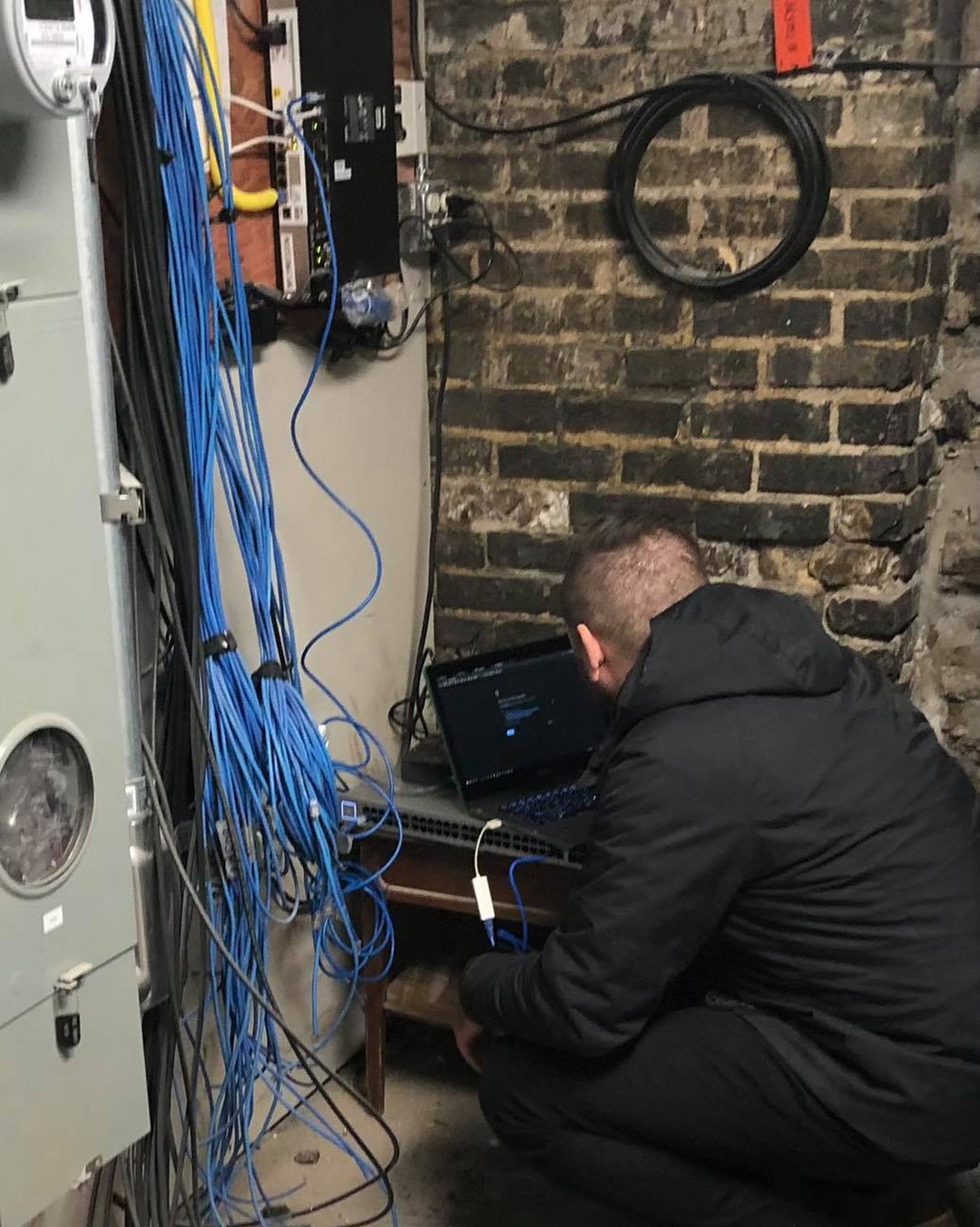 Technician splicing fiber internet in the 1889 coal room at Oaklands on 9th, cables running across original brick walls