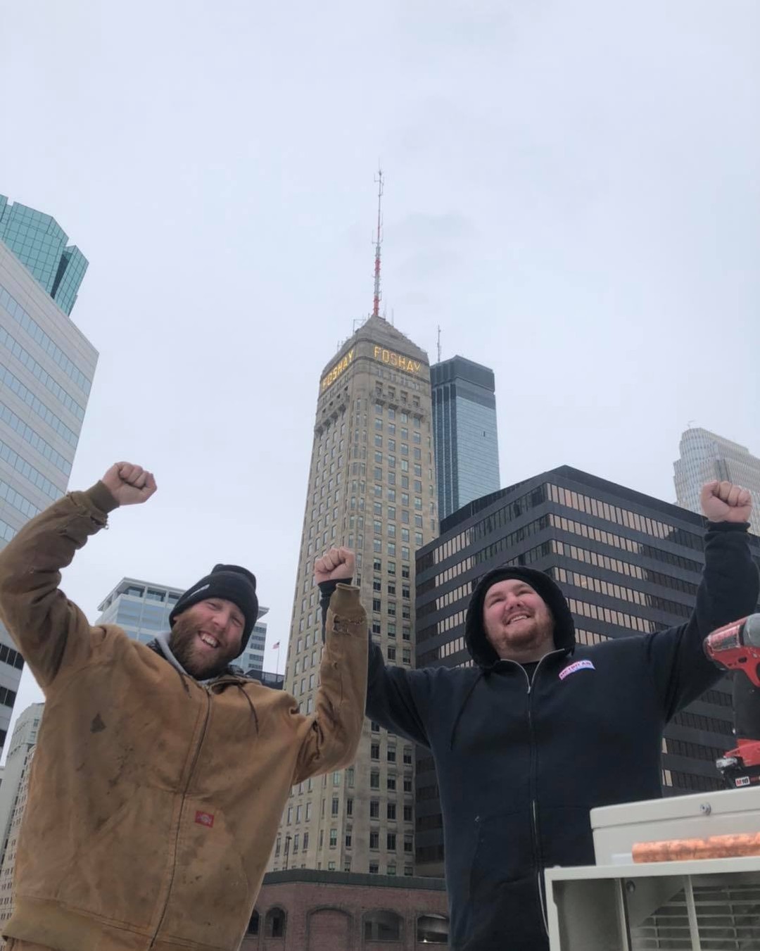 HVAC installers celebrating on the Oaklands on 9th rooftop after passing inspection, with the Foshay Tower behind them