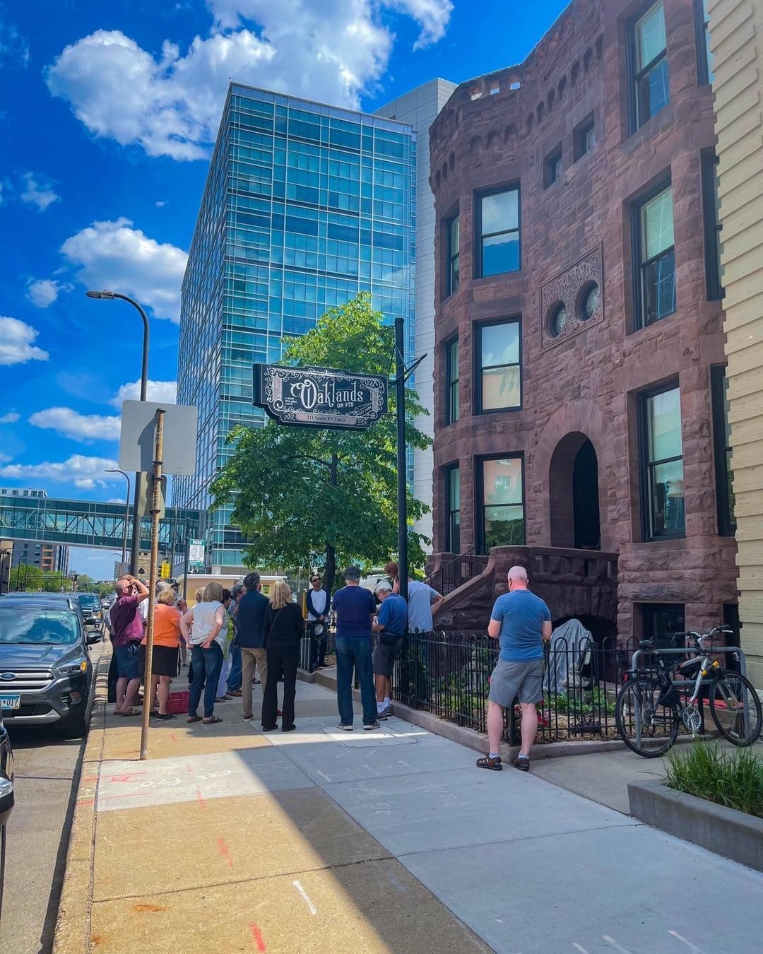 Guests walking the sunny South 9th Street sidewalk outside the restored 1889 brownstone facade of Oakland’s on 9th in downtown Minneapolis.