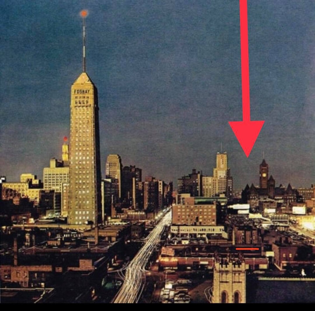 1959 photo of downtown Minneapolis at dusk with the Foshay Tower rising above 9th Street; a red arrow marks the Oaklands building