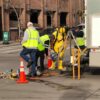 Minneapolis city crew in a yellow confined-space suit at a tripod winch over an open manhole in 9th Street, January 2021.