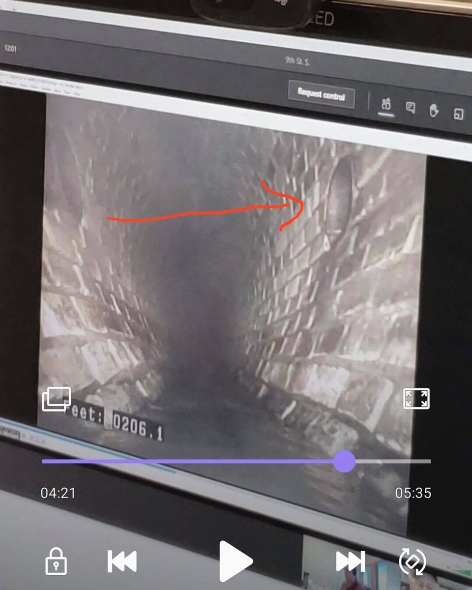 Sewer camera monitor showing the wet brick walls of the 1883 egg sewer under 9th Street, a red arrow marking the Oaklands drain.